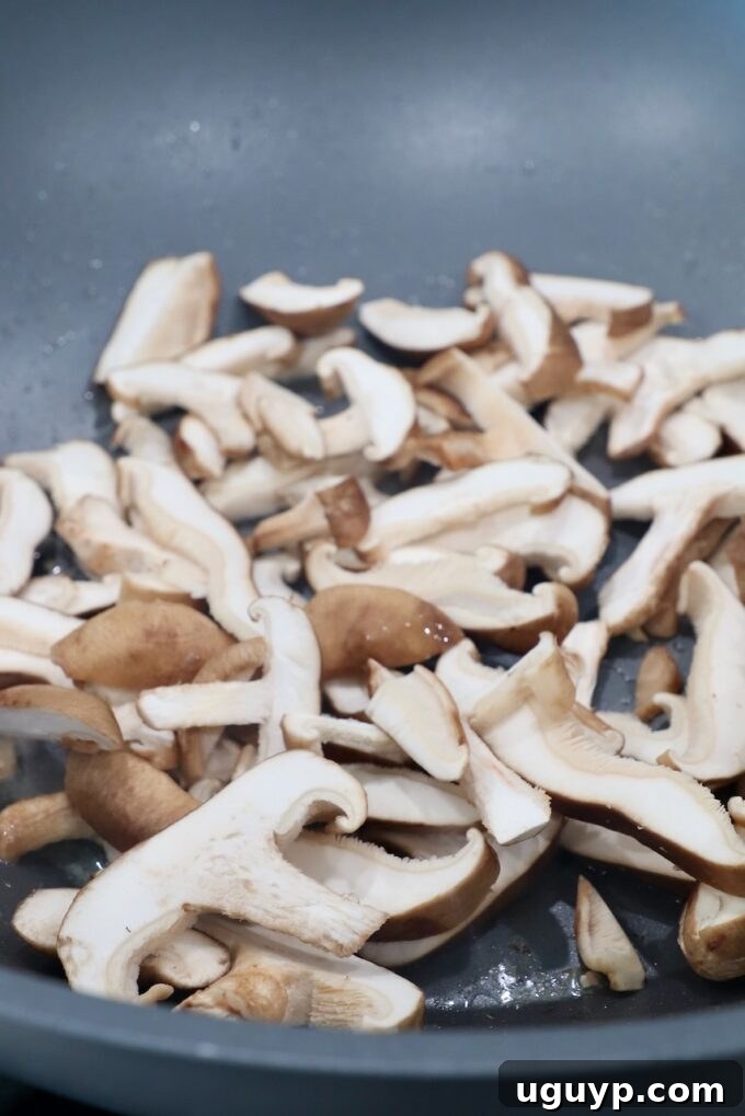 Sliced shiitake mushrooms being added to the wok, ready to absorb the flavors.