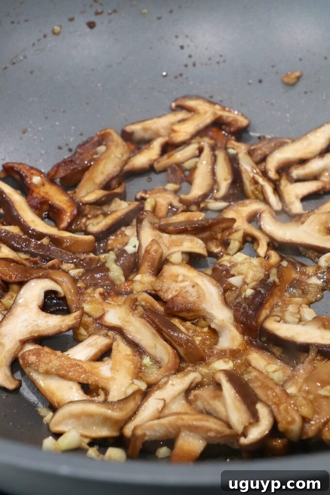 Cooked shiitake mushrooms glistening in the wok after being sautéed, ready for the aromatics.