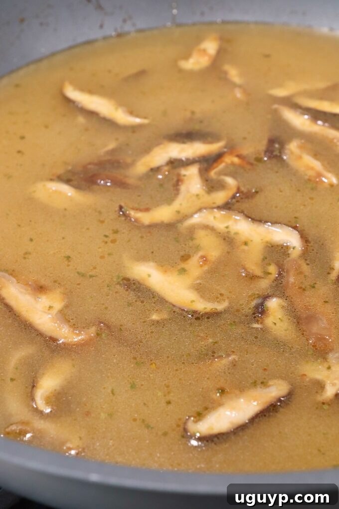 Aromatic broth with sliced mushrooms simmering in a large wok, showcasing the developing flavors.