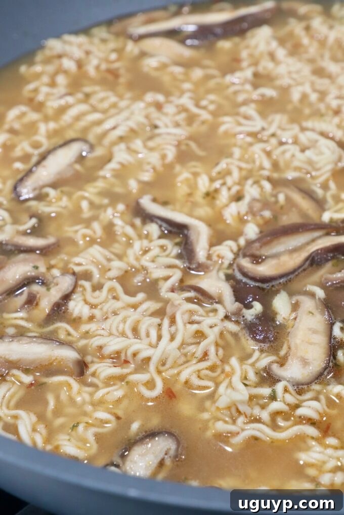 Ramen noodles being added to the simmering broth and mushrooms in the large wok.