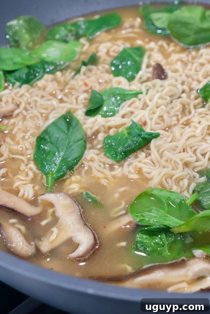 Fresh spinach leaves and cooked pork being stirred into the ramen noodles and broth in the wok, completing the dish.