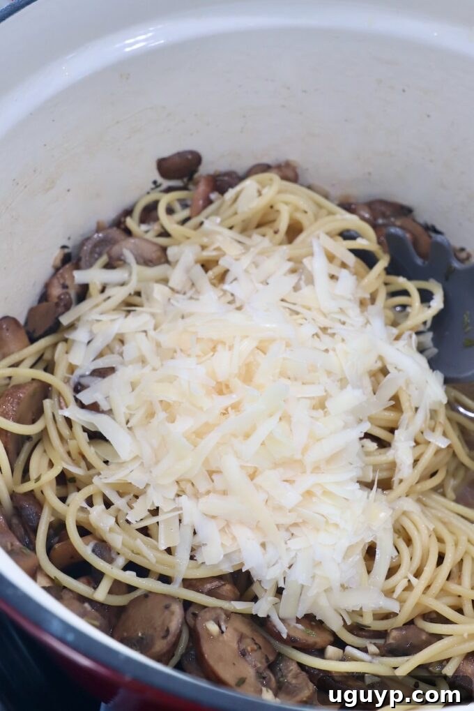 Cooked spaghetti and fresh Parmesan cheese added to the mushroom sauce, ready to be tossed.