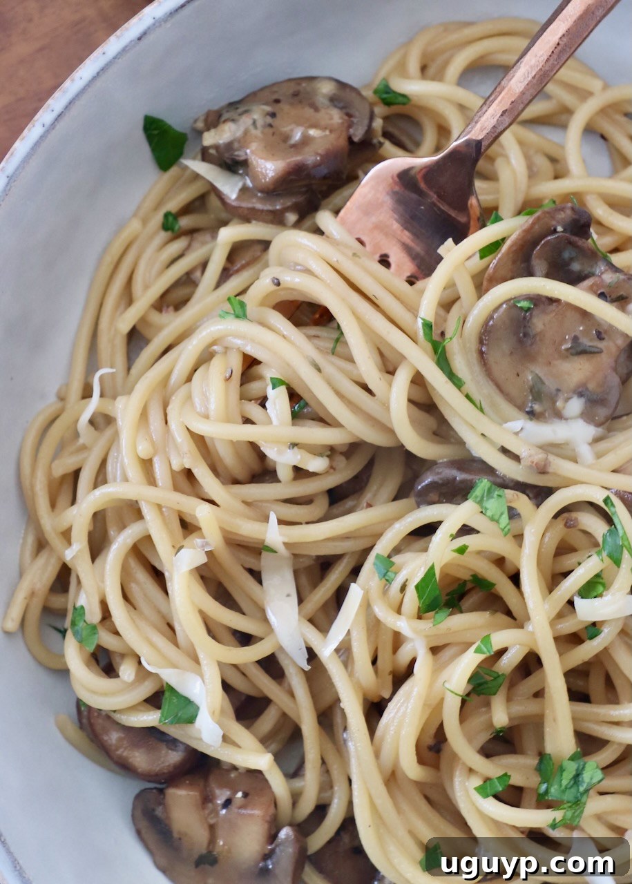 A close-up of garlic mushroom spaghetti in a bowl with a fork, garnished with fresh herbs.