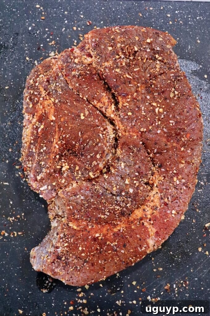 A generously seasoned chuck roast resting on a cutting board, ready for the smoker.