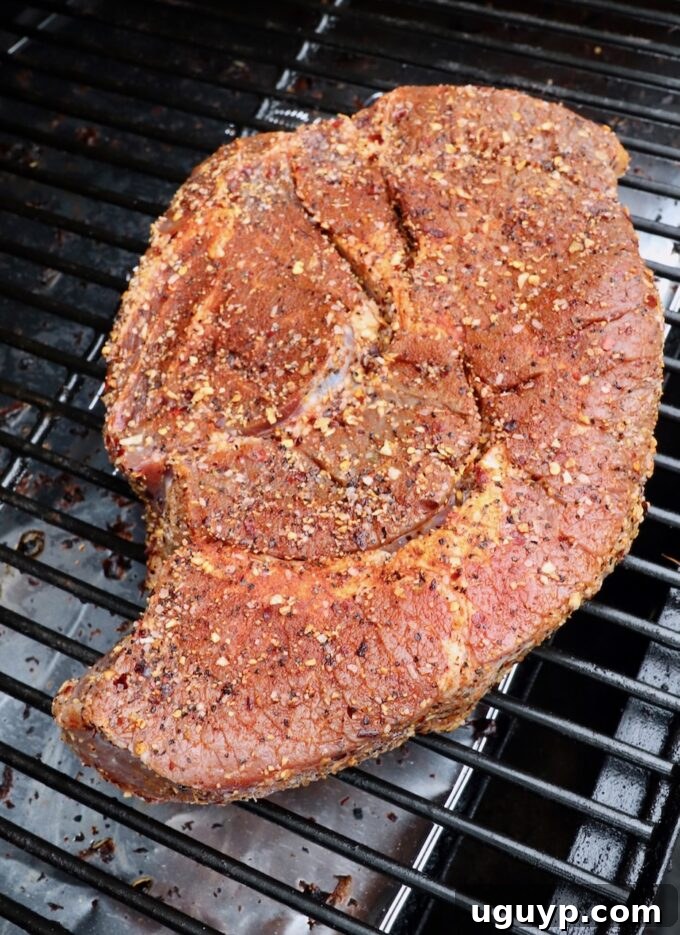 Seasoned chuck roast positioned on the smoker grates, beginning its low-and-slow cook.