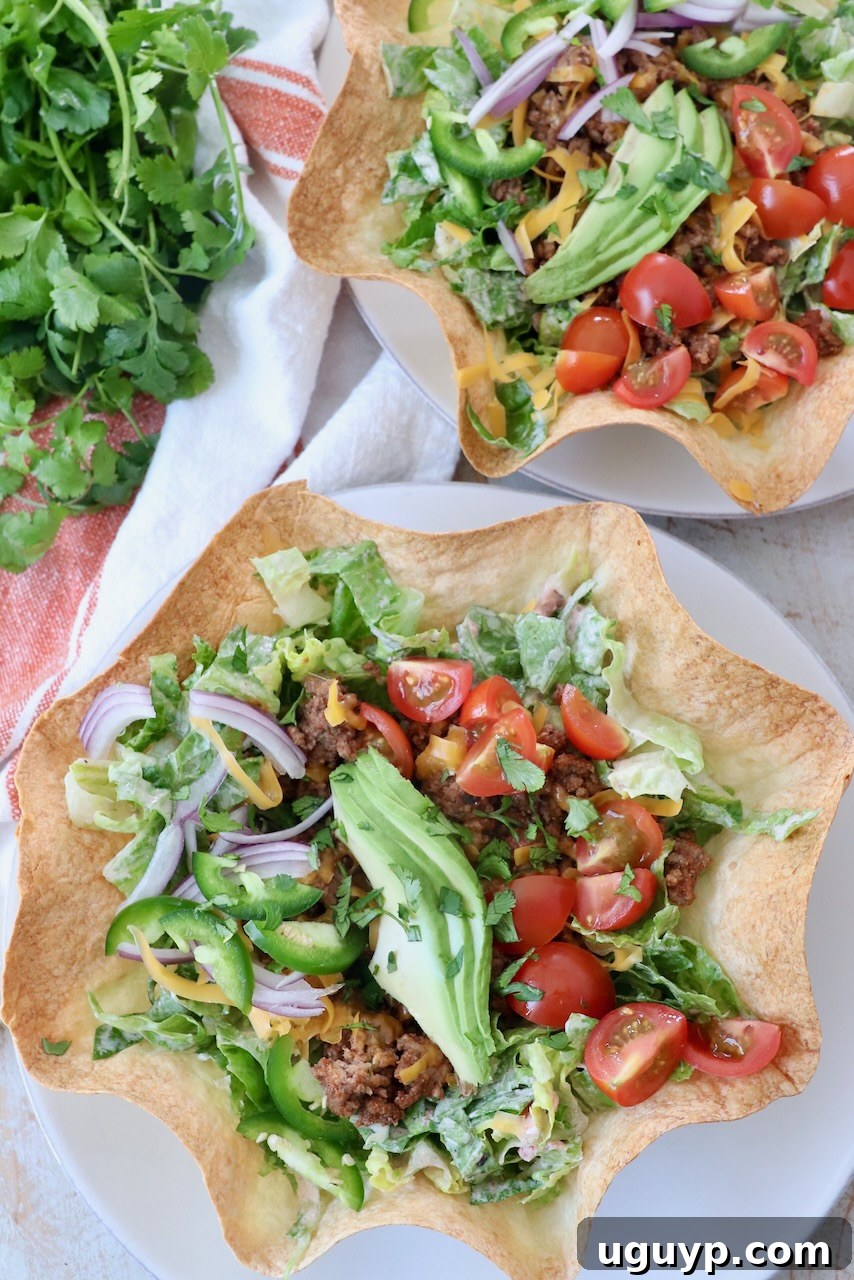 Delicious taco salad served in a crispy tortilla bowl, garnished with fresh avocado slices, on a clean white plate.