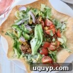 Taco salad in a crispy tortilla shell on a white plate, showcasing a delicious and ready-to-eat meal.
