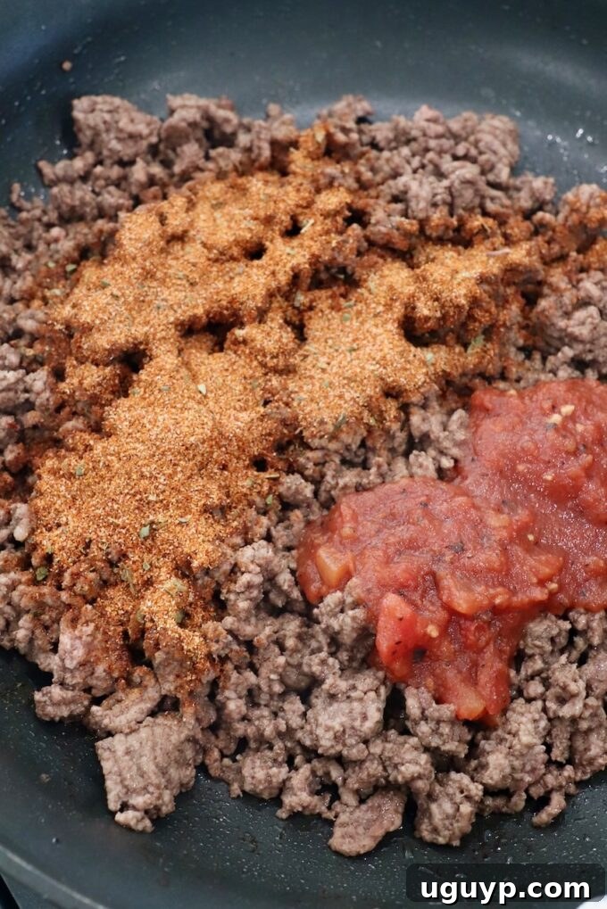Seasoned ground beef with taco seasoning and salsa simmering in a large skillet on the stove.
