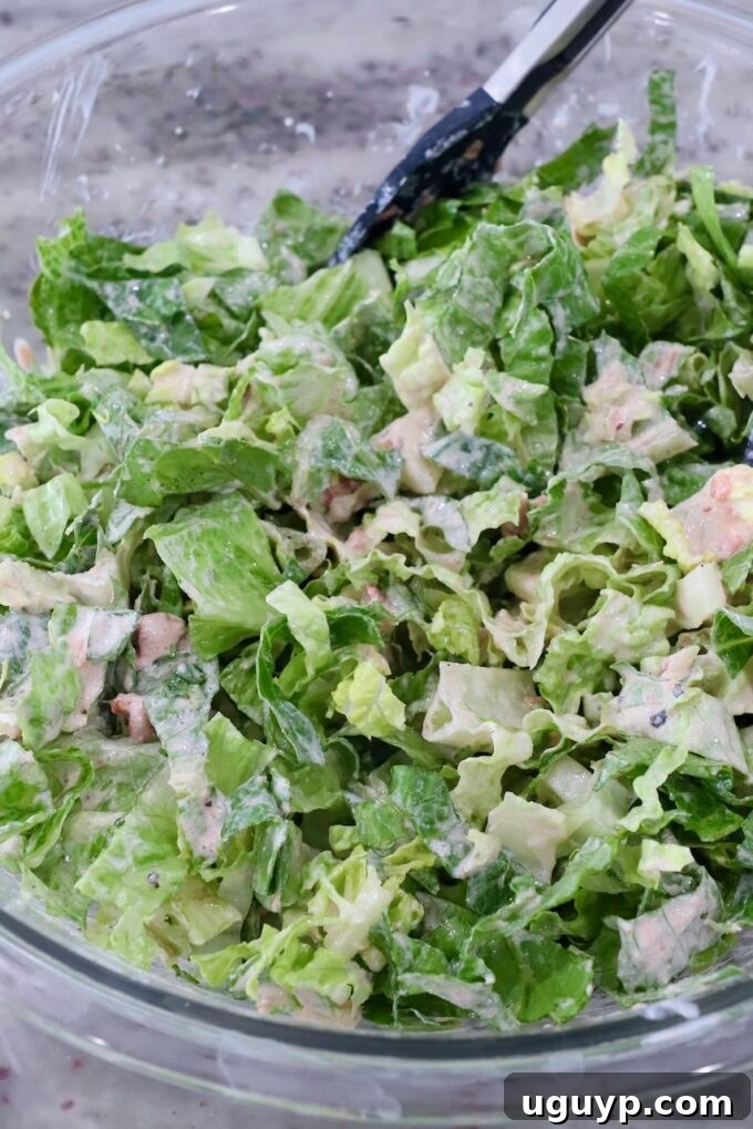 Shredded lettuce being tossed with the creamy taco salad dressing in a large glass bowl.