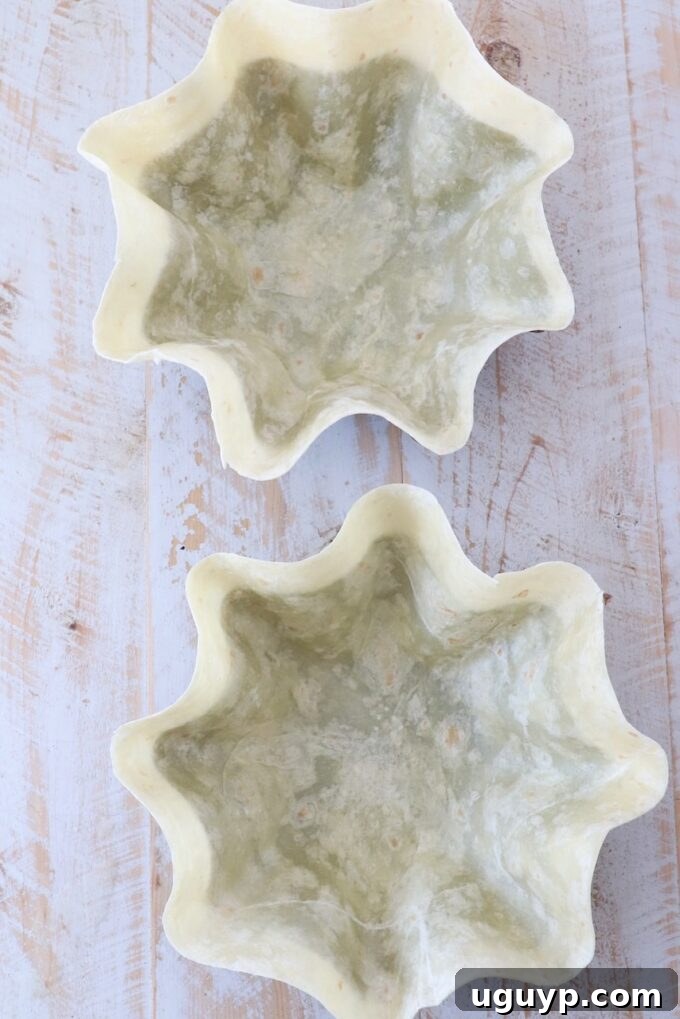 Large flour tortillas pressed into metal taco shell pans, ready for baking to create crispy bowls.