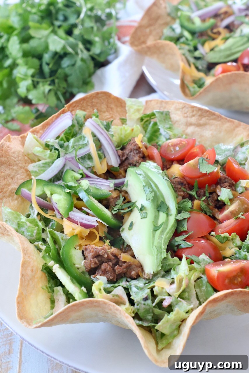 A vibrant taco salad neatly arranged in a crispy tortilla shell bowl, presented on a white plate, highlighting its fresh ingredients and inviting presentation.