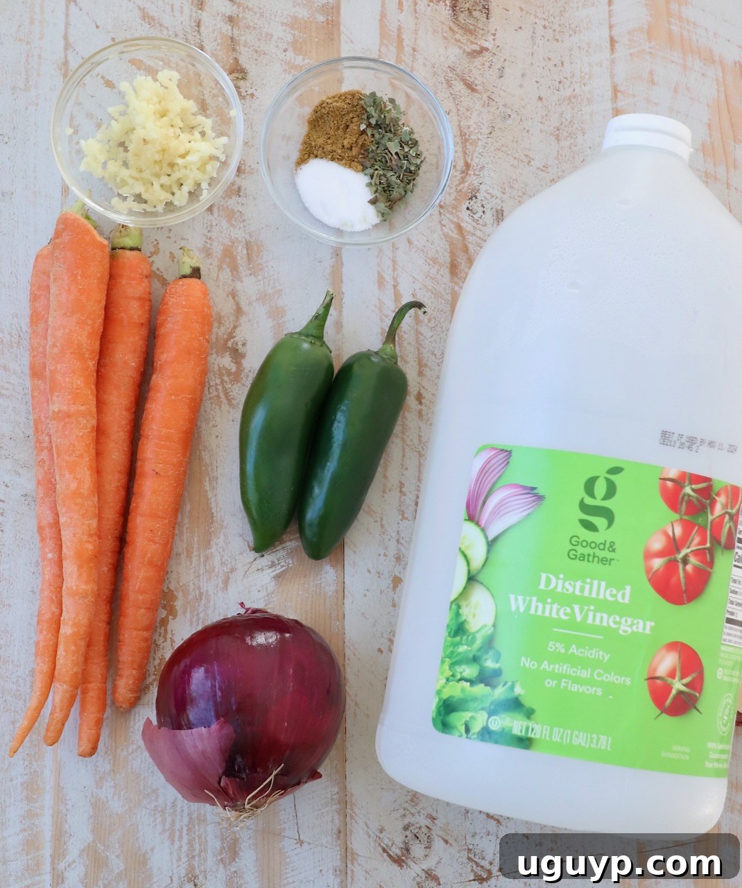 A selection of fresh ingredients laid out on a white wooden board, including thinly sliced red onions, carrots, and vibrant green jalapenos, ready for preparing Mexican Pickled Vegetables.