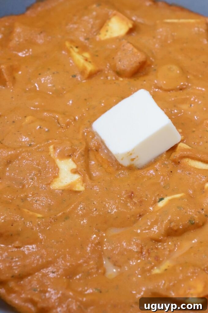 Finished Paneer Makhani in a large pan, topped with a cube of butter and a swirl of heavy cream, ready to be served.