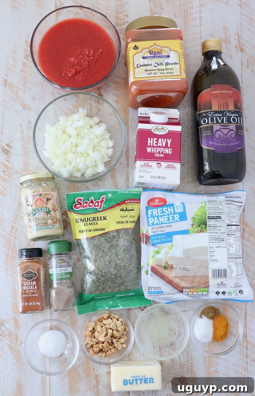 A collection of fresh ingredients for Paneer Makhani arranged beautifully on a white wooden board, including onions, tomatoes, cashews, and various spices.