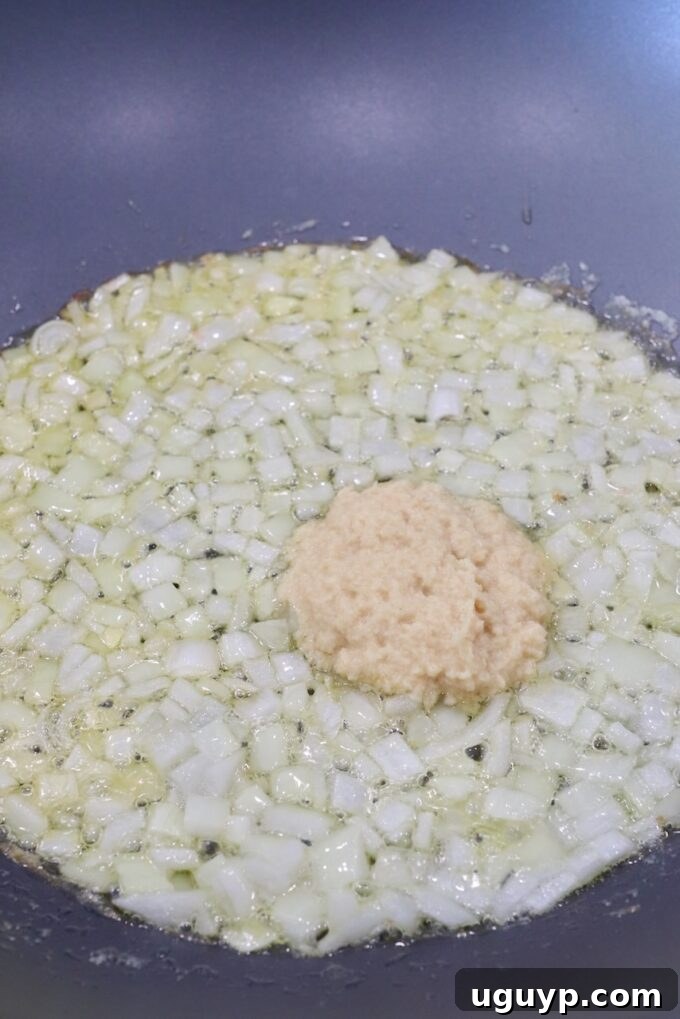Diced onions sautéing in a large skillet with ginger garlic paste, beginning to soften and release their aromatic flavors.