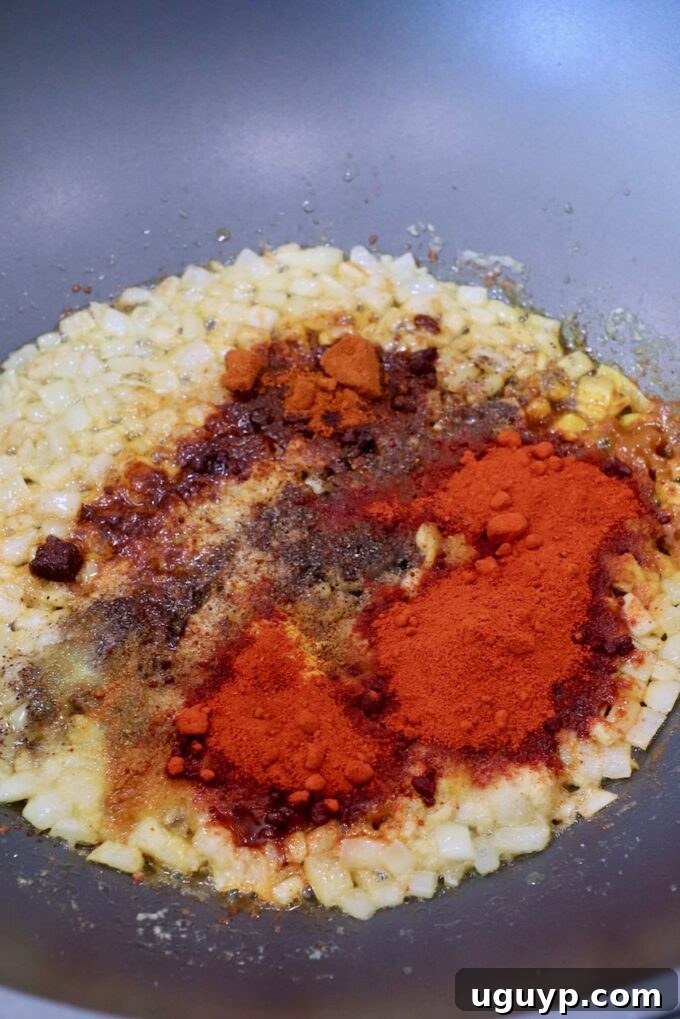 Aromatic Indian spices, including garam masala, chili powder, and turmeric, added to sautéed onions in a large skillet, releasing their fragrance.