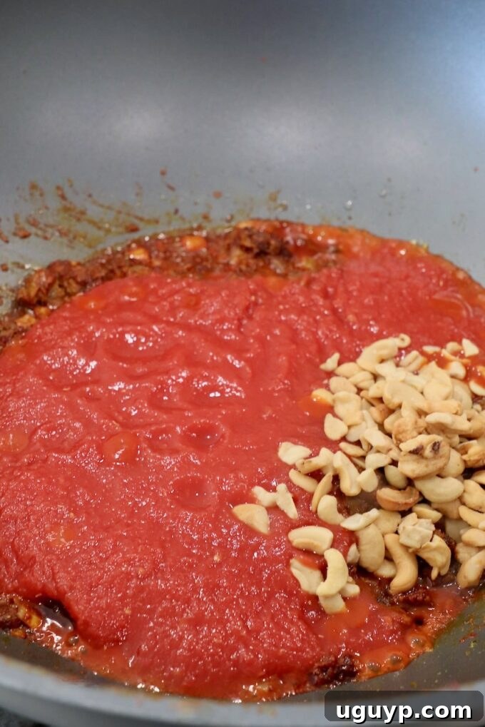 Crushed tomatoes and cashews added to the skillet with cooked spices and onions, forming the rich base of the curry sauce.