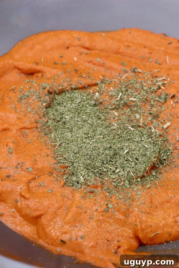 A rich curry sauce in a large pan, with dried fenugreek leaves added, infusing it with their distinctive aroma.