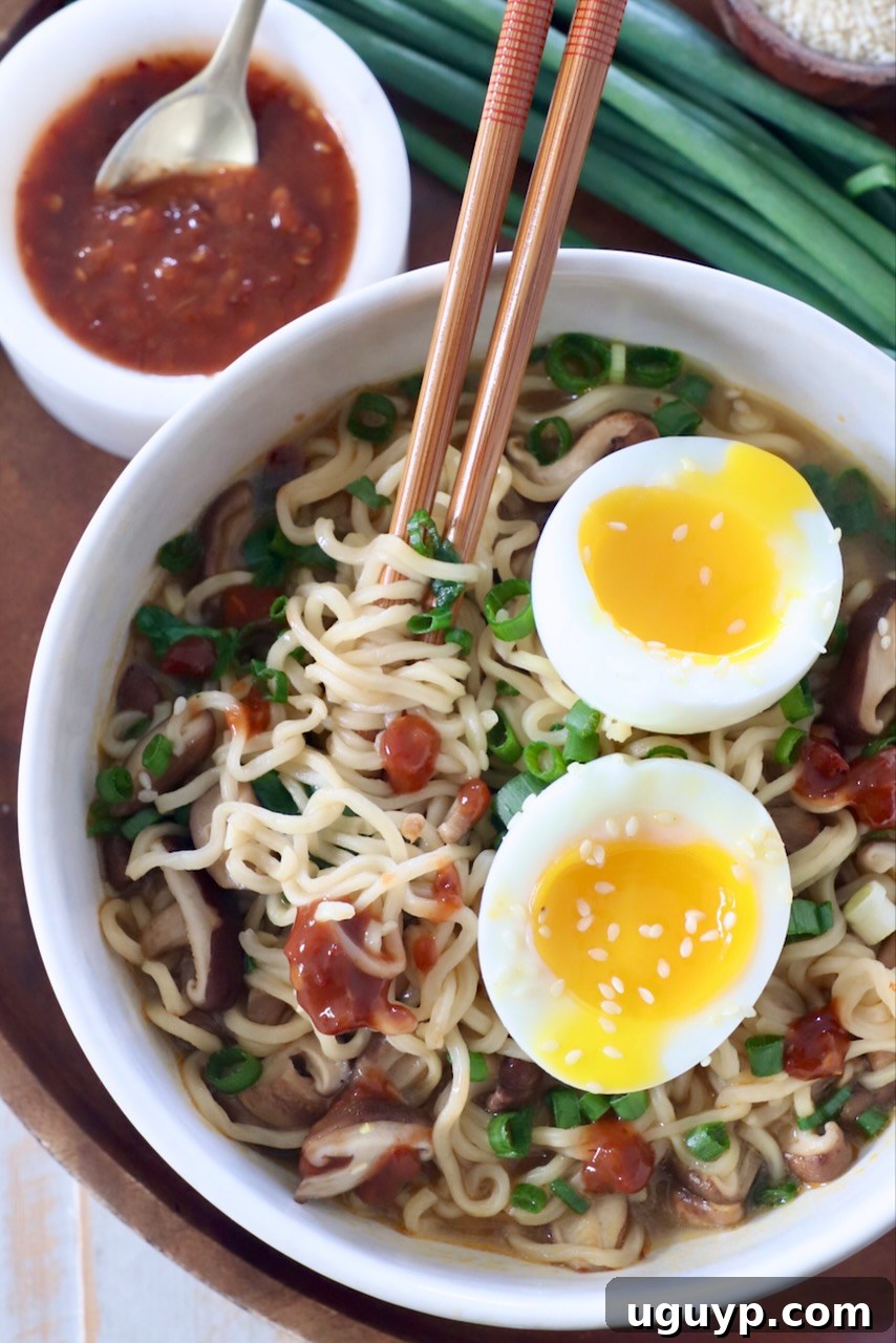 A steaming bowl of Vegetarian Ramen, topped with a perfectly soft-boiled egg cut in half, invitingly presented with chopsticks.