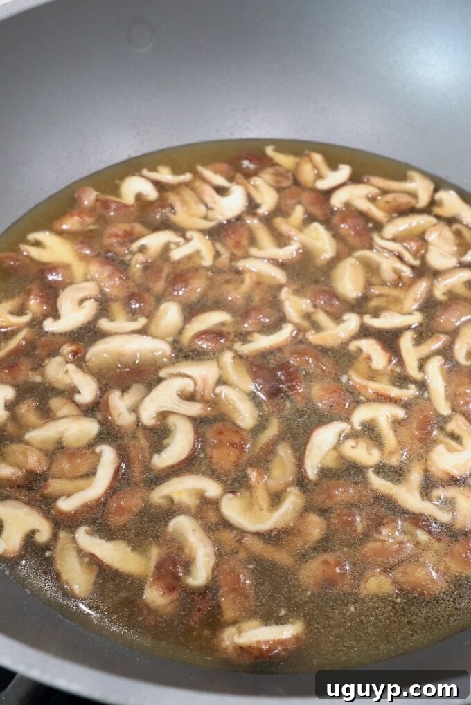 Thickly sliced shiitake mushrooms sizzling in sesame oil and soy sauce within a large pot on the stove, developing a golden color.