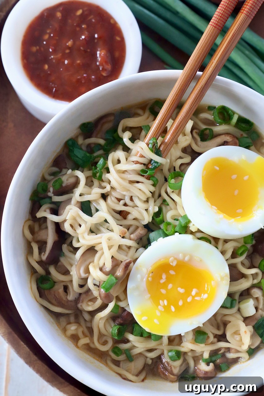 A beautifully presented bowl of homemade ramen noodle soup with chopsticks, featuring a soft-boiled egg, fresh green onions, and vibrant broth.