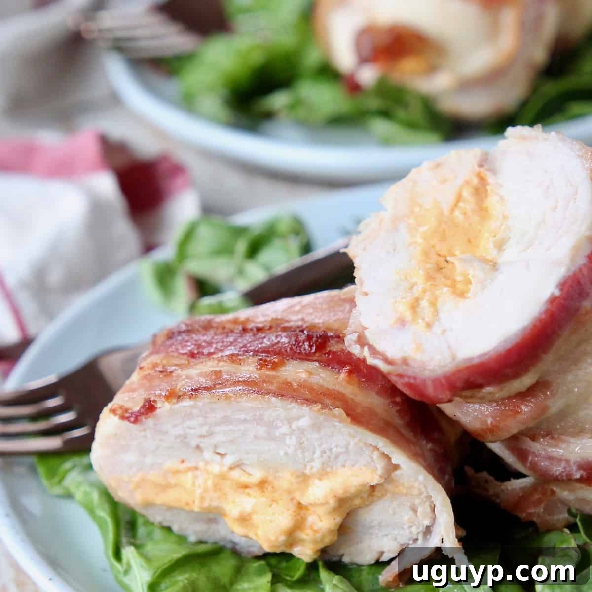 A perfectly cooked bacon-wrapped stuffed chicken breast, sliced in half to reveal its creamy filling, served on a plate.