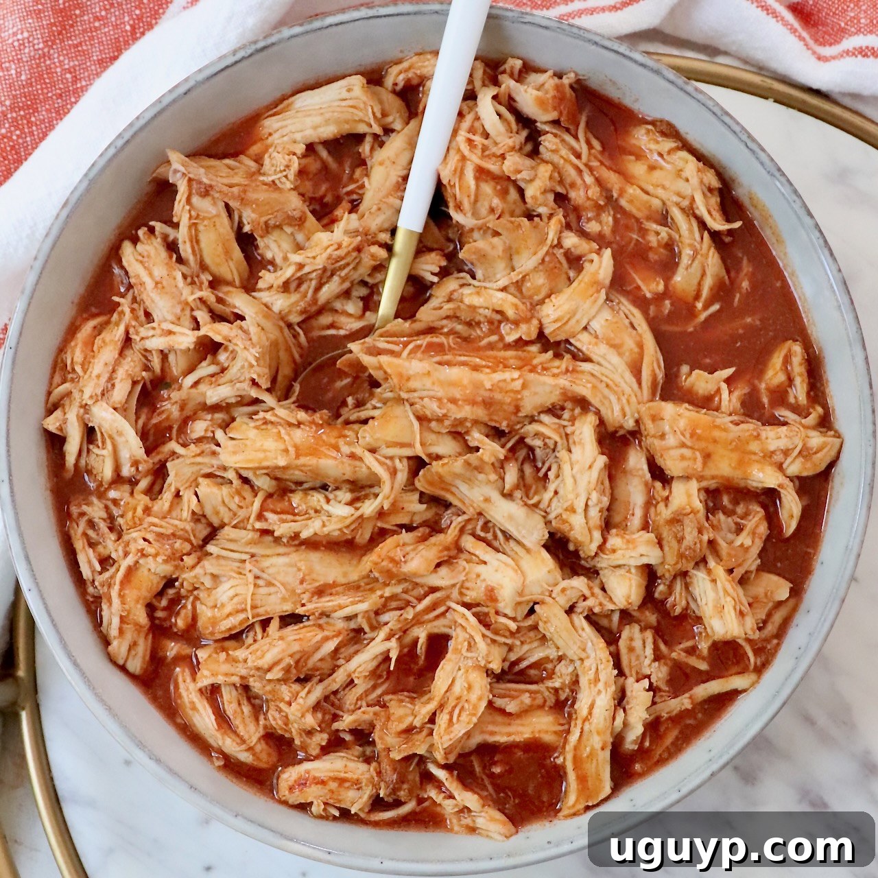 A bowl of flavorful shredded buffalo chicken, drenched in sauce, with a fork ready to serve.
