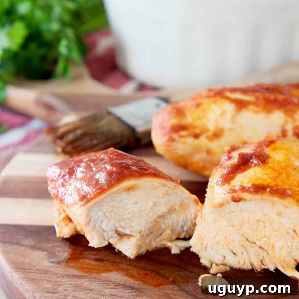 Succulent baked chicken covered in a rich BBQ and buffalo sauce, with one piece sliced on a wooden cutting board.