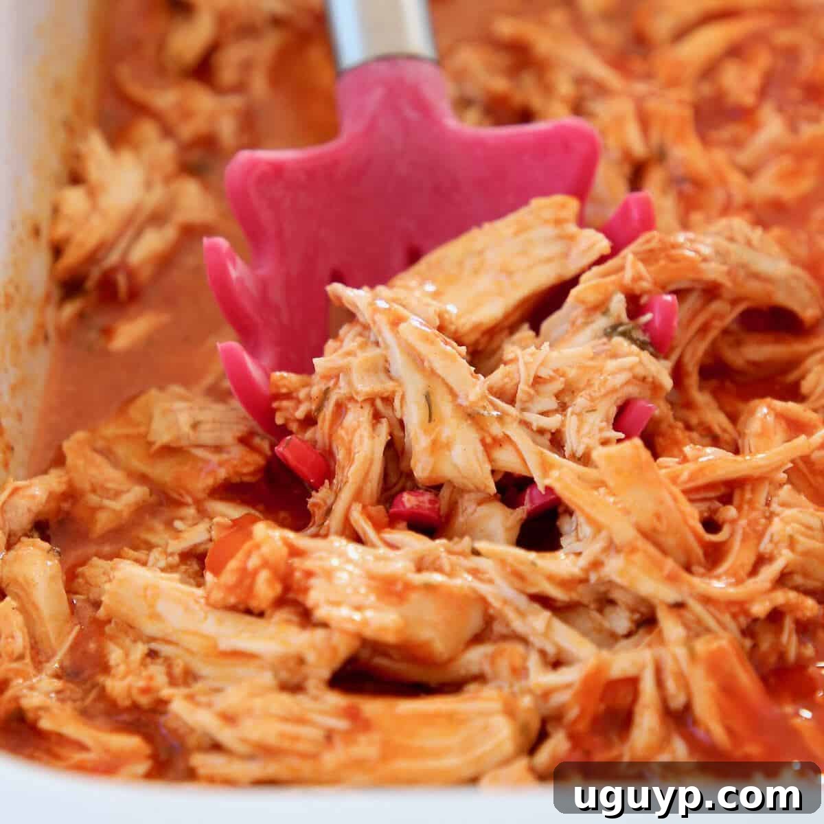 A bowl of perfectly shredded buffalo chicken with a red serving spoon, ready to be incorporated into various dishes.