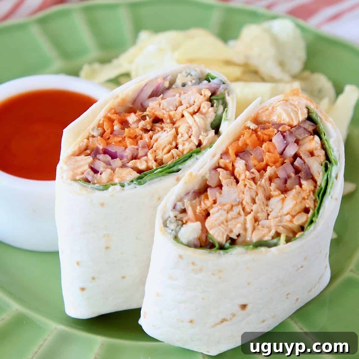 Two halves of a buffalo chicken wrap, standing upright on a vibrant green plate, showcasing the delicious filling.