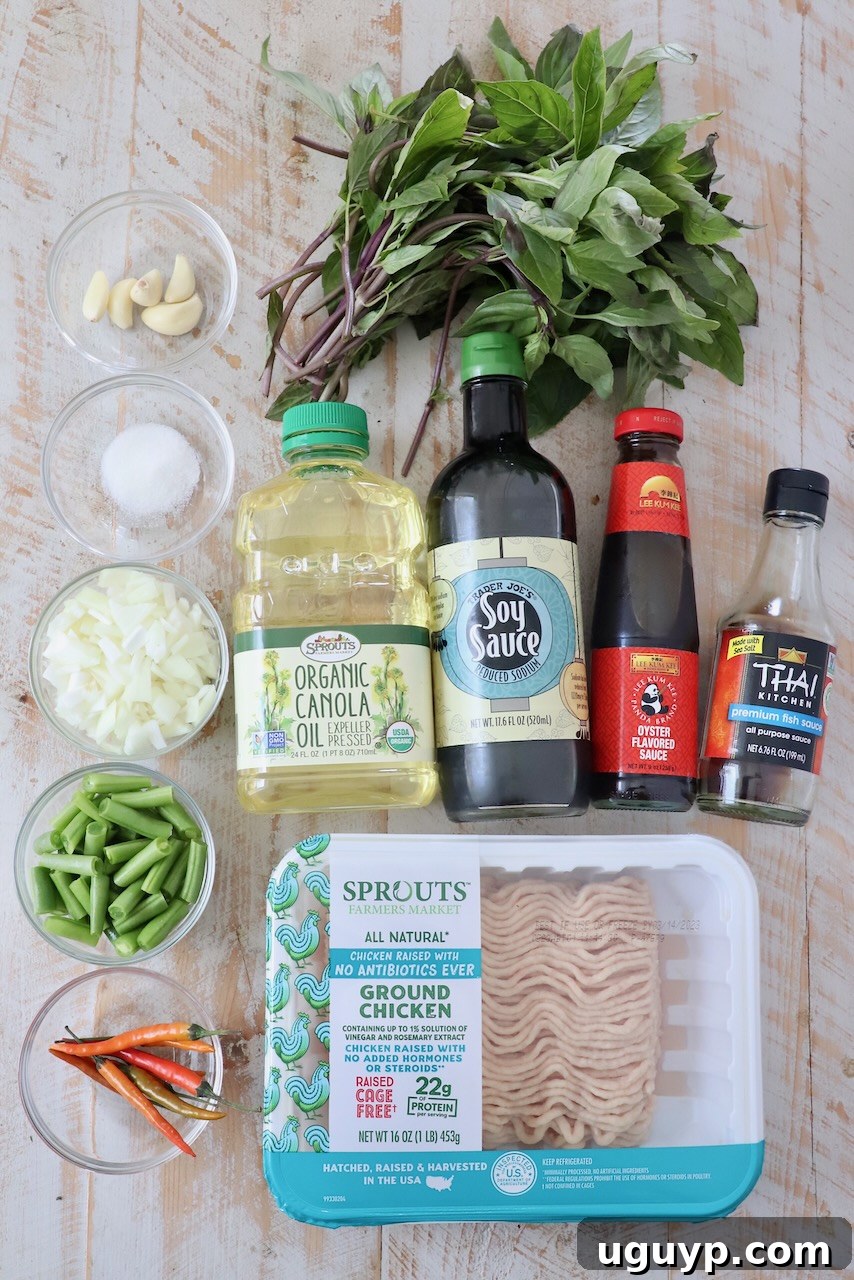 A collection of fresh ingredients for Thai Basil Chicken (Pad Krapow Gai) displayed on a white wooden board, including ground chicken, green beans, onions, garlic, chilies, and fresh Thai basil leaves.
