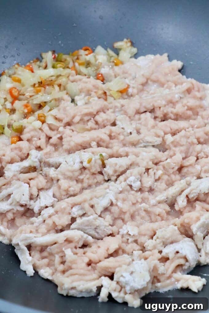 Ground chicken and vegetables (onions, green beans) cooking in a large skillet or wok, sizzling and browning, forming the base of the Thai Basil Chicken dish.