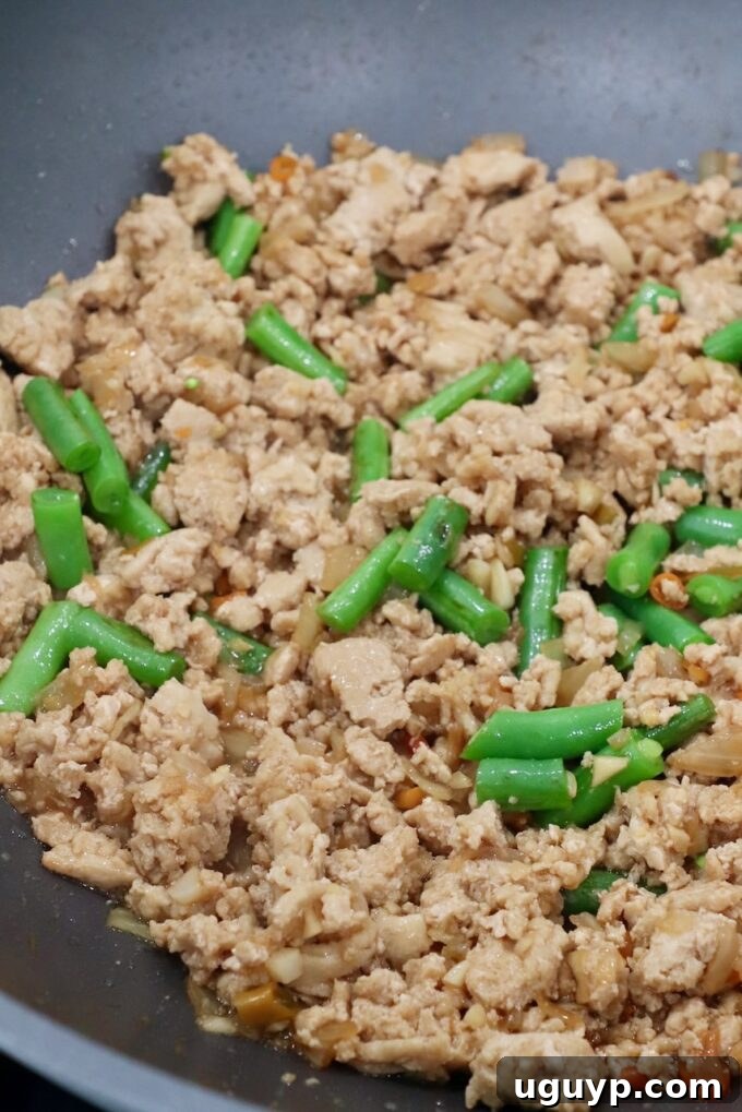 Cooked ground chicken mixed with green beans in a large pan, ready for the sauce to be added and integrated.