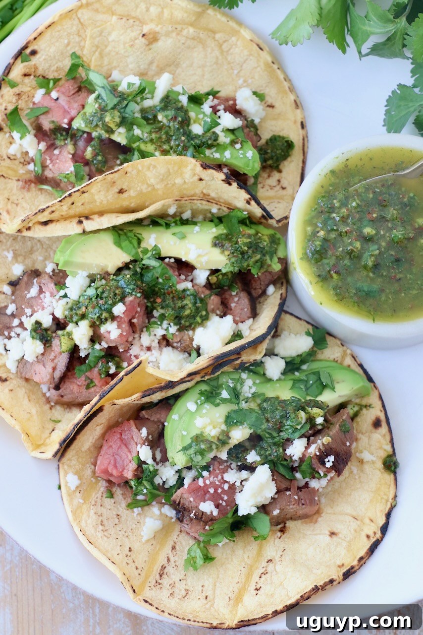 three tacos on plate filled with grilled steak, avocado and chimichurri sauce