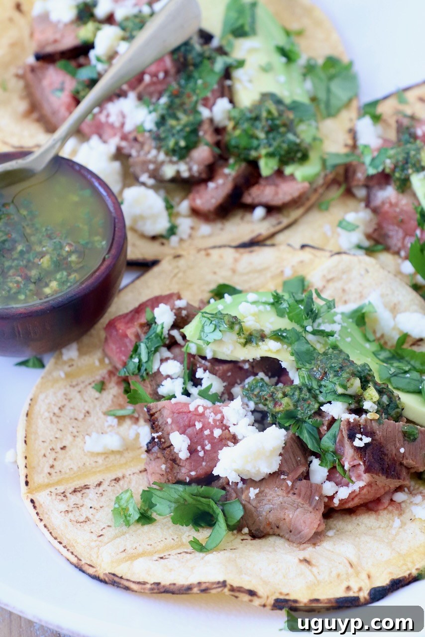 grilled steak in tortillas on plate topped with cotija cheese, avocado and chimichurri sauce