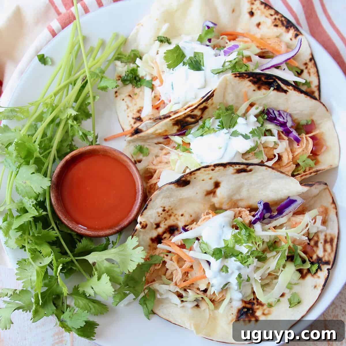 Tacos on plate with small wooden bowl of buffalo sauce on the side