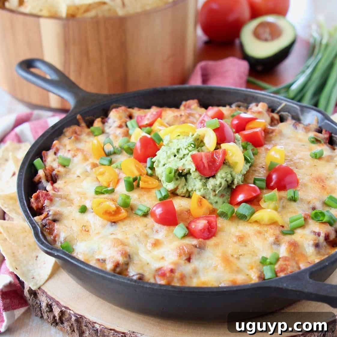 Baked taco dip in a cast iron skillet, sitting on a wood cutting board with a bowl of chips in the background