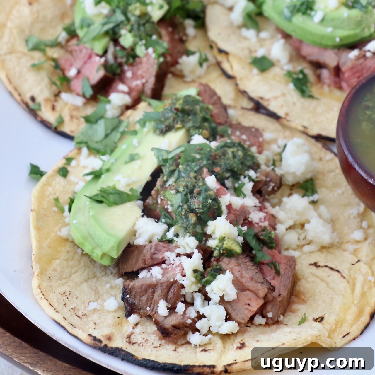 grilled diced steak in tacos with avocado and chimichurri sauce on white plate