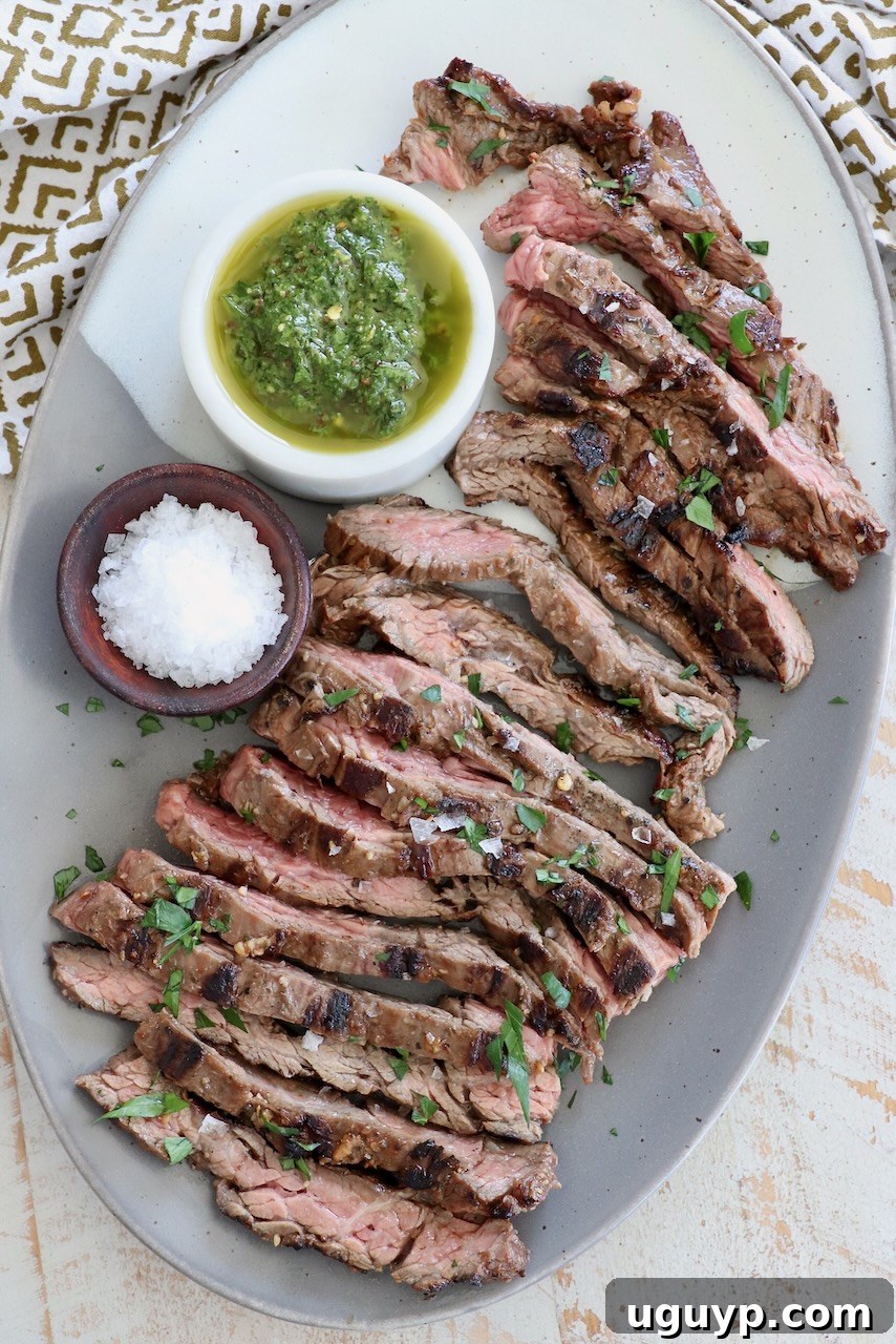 Sliced grilled skirt steak on a plate with small bowls of chimichurri sauce and flaky sea salt on the side