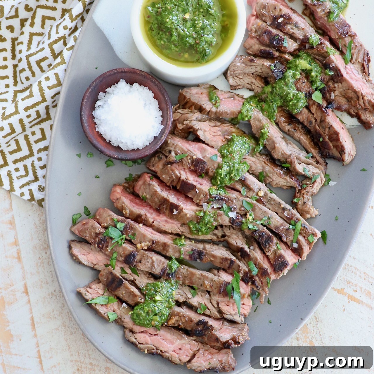 Sliced grilled skirt steak on a white plate, generously topped with fresh chimichurri sauce