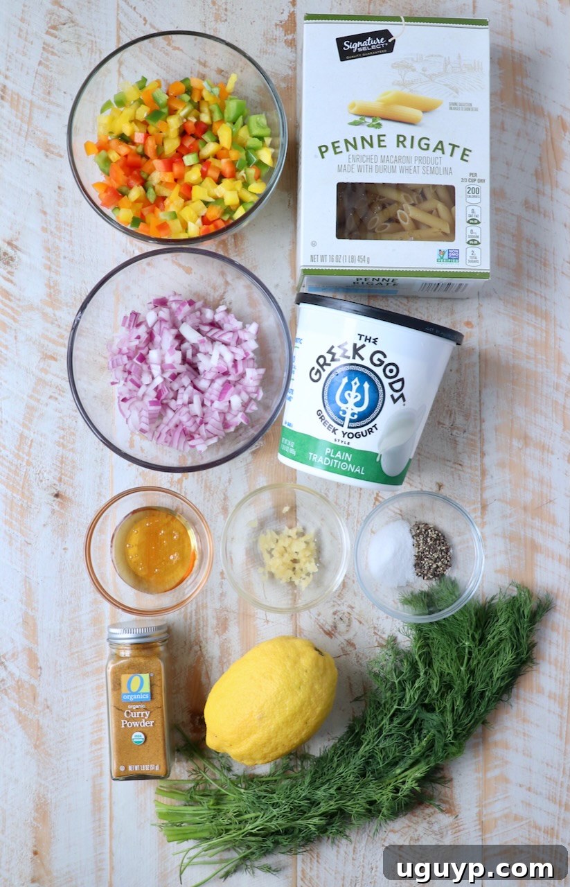 assorted fresh ingredients for pasta salad laid out on a white wooden board, including penne pasta, bell peppers, red onion, Greek yogurt, lemon, and fresh dill