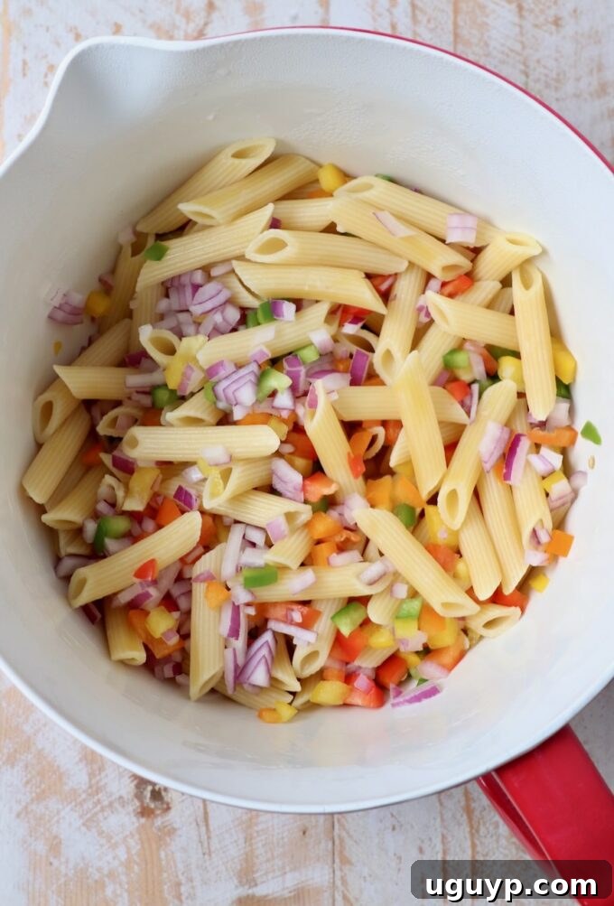 cooked penne pasta and freshly diced bell peppers and red onion in a large mixing bowl, awaiting the dressing