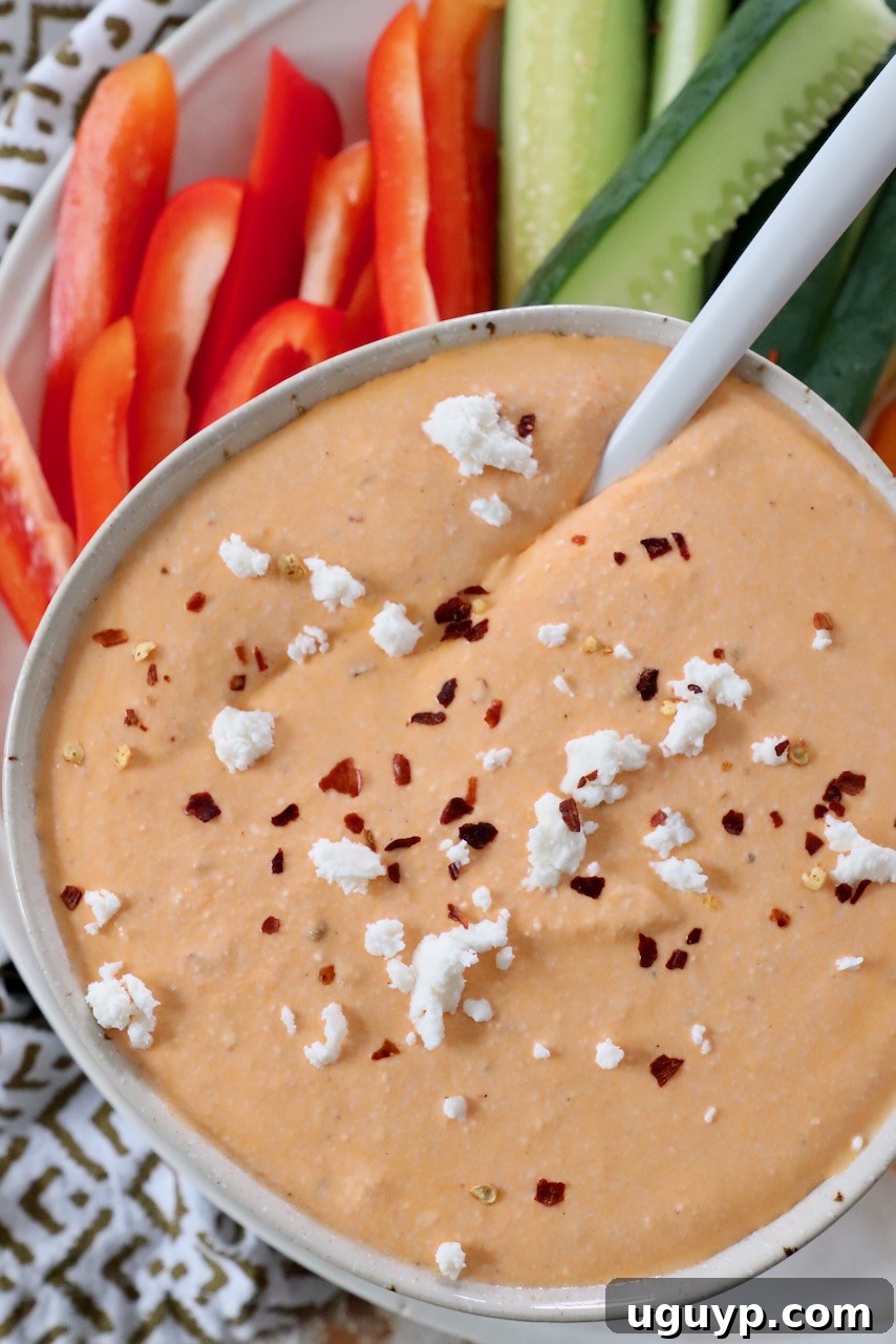 Creamy spicy whipped feta dip in a rustic bowl, garnished with a sprinkle of red pepper flakes and a fresh herb, with a spoon ready for dipping.