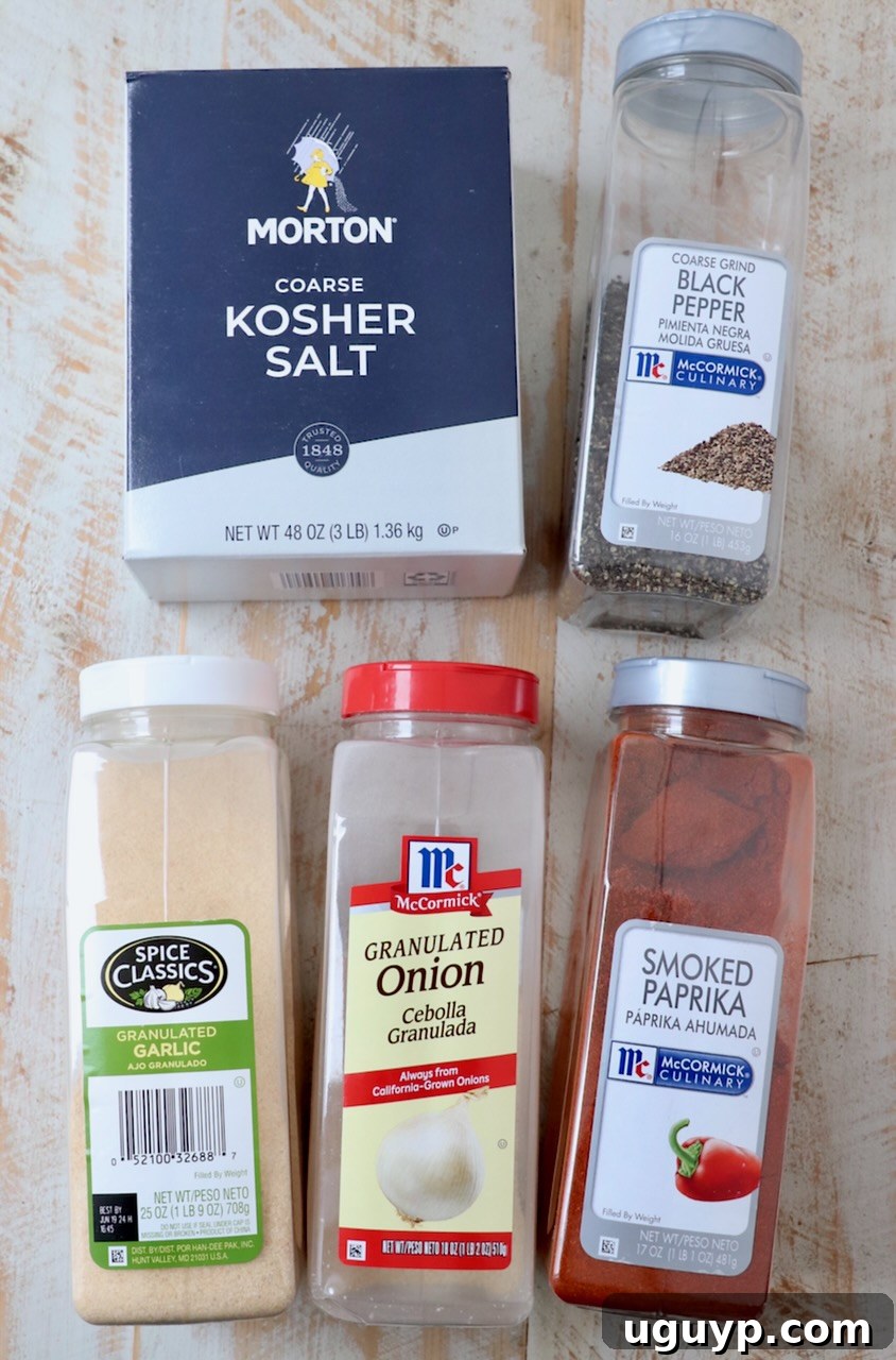 Ingredients for a homemade pulled pork rub laid out on a white wooden board, including coarse salt, pepper, and paprika.