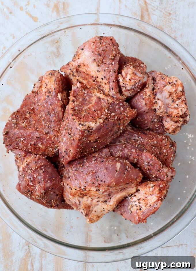 Large pieces of pork shoulder seasoned thoroughly in a glass bowl