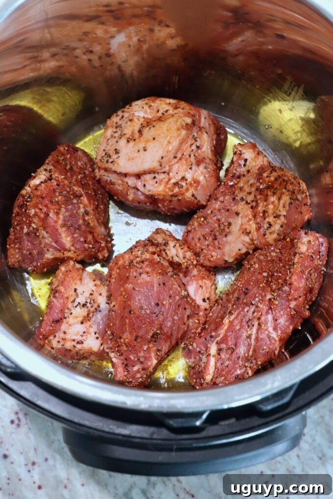 Large pieces of seasoned pork searing in olive oil in an Instant Pot