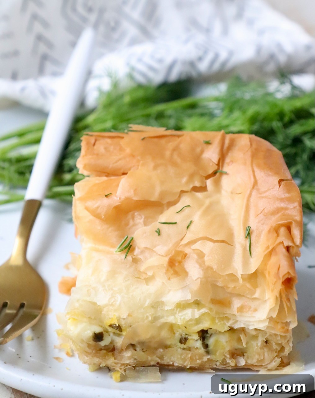 A delicious piece of Greek zucchini pie on a white plate with a fork, showing the golden phyllo layers and rich filling.