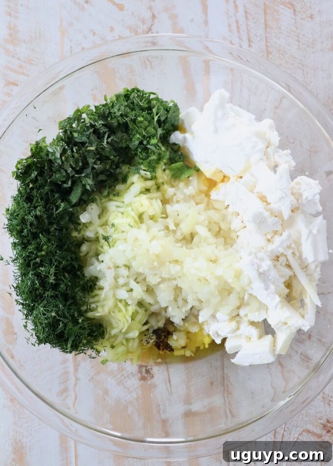 A large glass bowl filled with the colorful ingredients for the zucchini pie filling, including sautéed onions and garlic, ready to be mixed.