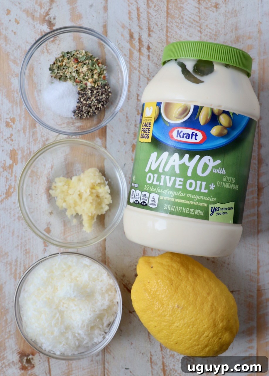 Ingredients for creamy Garlic Parmesan Sauce laid out on a white wooden board, including Parmesan cheese, mayonnaise, garlic, and herbs.