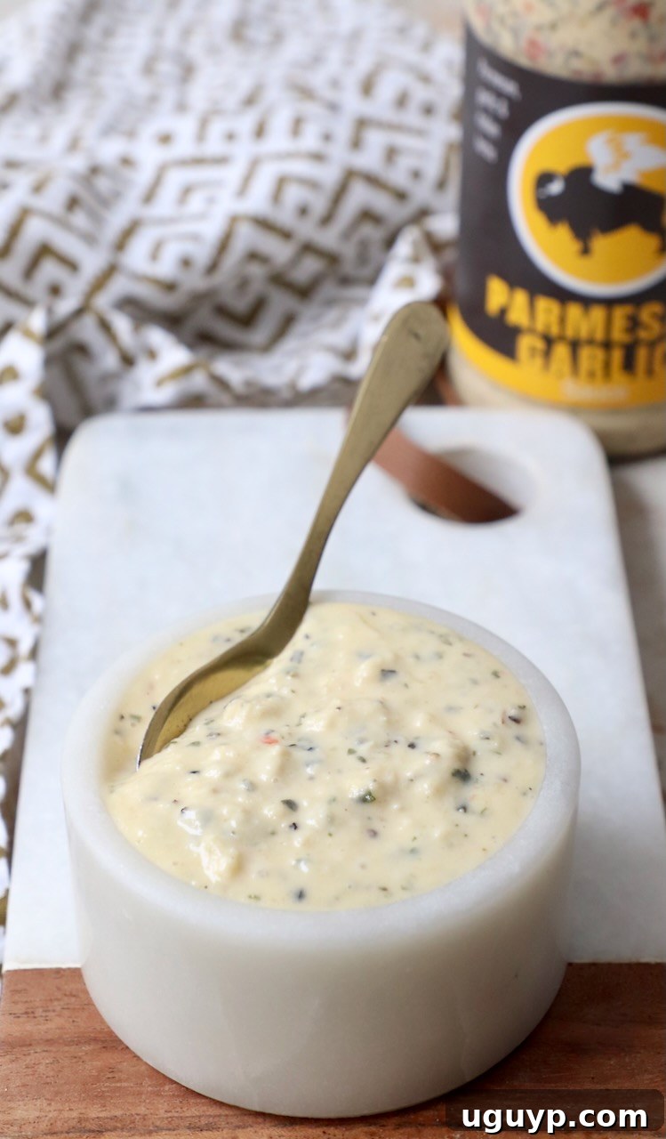 Close-up of creamy Garlic Parmesan Sauce in a small white bowl with a spoon, highlighting its smooth texture.